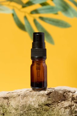 Kahverengi cam şişe ve şeker kutusu taşın üzerinde duruyor, sarı arka plan.