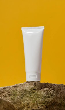 Beyaz plastik tüp sarı arkaplanda bir taşın üzerinde duruyor. Kozmetik ve diş macunu konteynırı