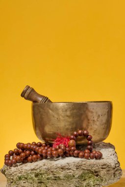 Bakır şarkı kasesi, tahta sopa ve taşa dua boncukları, sarı arka plan. Meditasyon ve rahatlama, alternatif tıp