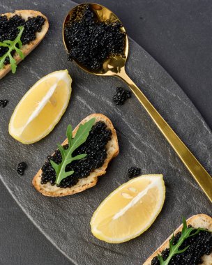 Siyah tabakta siyah mersin balıklı havyar ve limon dilimleri.