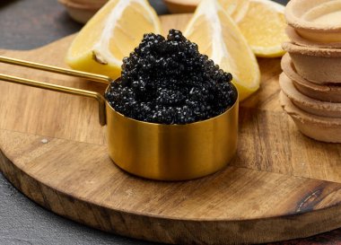 Bakır kasede siyah mersin balığı havyarı, limon dilimleri ve masada boş turtalar, kapatın.