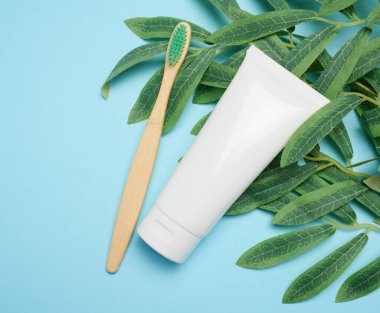 Mavi arka planda beyaz plastik tüp ve bambu diş fırçası.