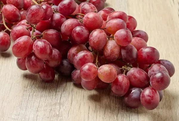 Masanın üzerinde bir demet olgun kırmızı üzüm var.