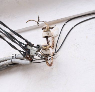 Eski elektrik kabloları ve seramik yalıtıcılar yıpranmış bir duvara bağlı.