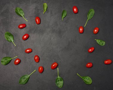 Dağınık ıspanak yaprakları ve siyah arkaplanda kırmızı kiraz domatesleri.