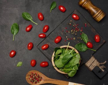 Taze ıspanak yaprakları, kiraz domatesleri ve siyah arka planda karışık biberler. Üst görünüm