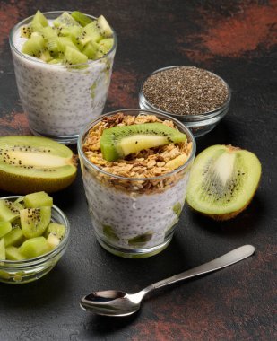 Koyu bir yüzeye dilimlenmiş kivi soslu Chia tohumu pudingi yarım kivi, bir kase doğranmış kivi ve chia tohumu.