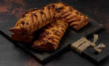 Altın rengi akçaağaç pekan cevizli örgü pastalar koyu dokulu bir yüzeye yerleştirilmiştir. Örülmüş hamur pul pul ve cevizlerle kaplı.