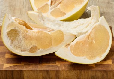 Görünür hamurlu ve kabuklu taze, sulu bir meyve dilimi. Tahta masanın üzerinde turunçgiller var.