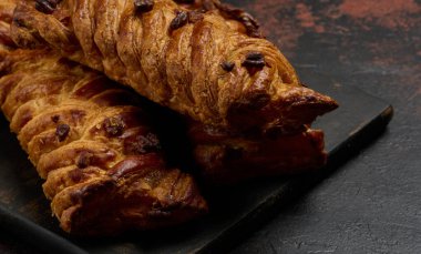 Altın rengi akçaağaç pekan cevizli örgü pastalar koyu dokulu bir yüzeye yerleştirilmiştir. Örülmüş hamur pul pul ve cevizlerle kaplı.