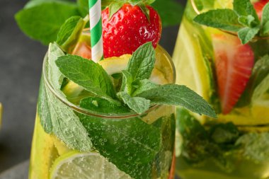Limon dilimleri, çilekler, taze nane yaprakları ve köpüklü suyla dolu bir bardakta ferahlatıcı bir içecek.