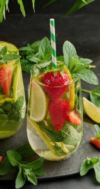 Limon dilimleri, çilekler, taze nane yaprakları ve siyah bir tabakta limon ve nane ile servis edilen köpüklü su dolu bir bardakta ferahlatıcı bir içecek.