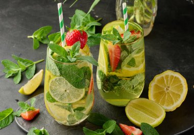 Limon dilimleri, çilekler, taze nane yaprakları ve köpüklü su dolu bir bardakta ferahlatıcı bir içecek.