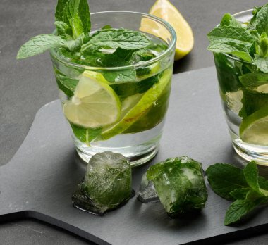 Koyu arkaplanda limon, nane ve buz ile mojito kokteylini tazeliyorum.