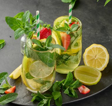 Limon dilimleri, çilekler, taze nane yaprakları ve köpüklü suyla dolu bir bardakta ferahlatıcı bir içecek.