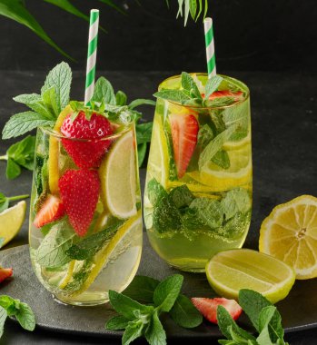 Limon dilimleri, çilekler, taze nane yaprakları ve siyah bir tabakta limon ve nane ile servis edilen köpüklü su dolu bir bardakta ferahlatıcı bir içecek.