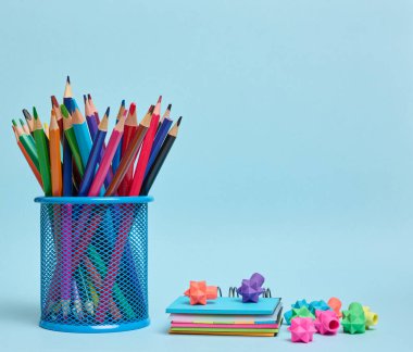 Kırtasiye seti bir bardağa renkli kalemler ve çalışmayı, organizasyonu veya yaratıcılığı, mavi arka planı simgeleyen bir silgi.