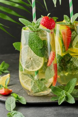 Limon dilimleri, çilekler, taze nane yaprakları ve köpüklü su dolu bir bardakta ferahlatıcı bir içecek.