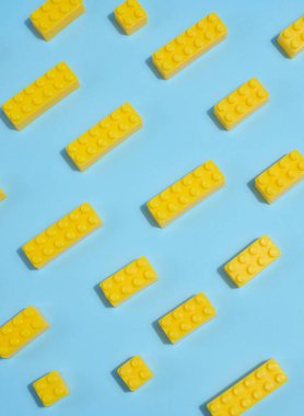 Mavi arka planda dağınık sarı plastik oyuncak yapı tuğlaları. Oyun, inşaat, eğitim veya yaratıcı konsept