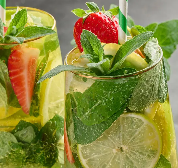 Limon dilimleri, çilekler, taze nane yaprakları ve köpüklü su dolu bir bardakta ferahlatıcı bir içecek.