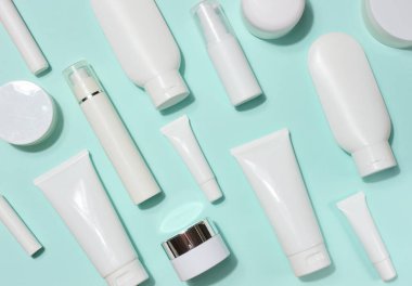 Çeşitli beyaz plastik tüpler ve kozmetik ürünler, açık mavi arka planda rastgele yerleştirilmiş. Üst görünüm