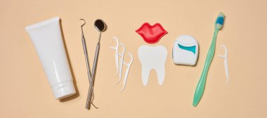Ağız hijyeni, diş macunu, diş ipi, diş ipi, kağıt diş ve kırmızı dudak şeklindeki dekoratif elementler, bej arkaplan.