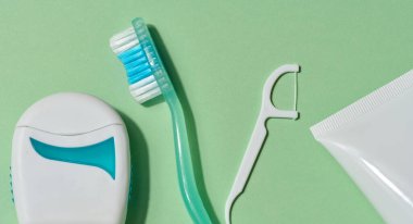 Yeşil diş fırçası, beyaz diş ipi dağıtıcısı, beyaz diş ipi penası ve bir tüp diş macunu, yeşil arka plan gibi çeşitli diş hijyen ürünlerinin düz bileşimi
