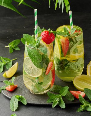 Limon dilimleri, çilekler, taze nane yaprakları ve köpüklü su dolu bir bardakta ferahlatıcı bir içecek.