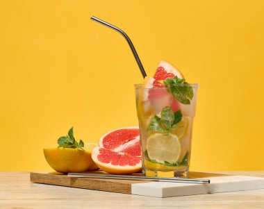İçinde kokteyl, greyfurt, limon ve portakal dilimleri ve metal pipet olan bir bardak. Sarı arkaplan