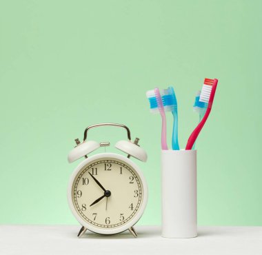 Beyaz antika çalar saat yeşil arka planda diş fırçaları ile ayakta duruyor. Hijyen, sabah ve program