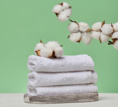 Bir yığın beyaz katlanmış havlu mermer bir standın üzerinde yatıyor, üstünde doğal pamuk cilt yüzeyi var. Yeşil arkaplan