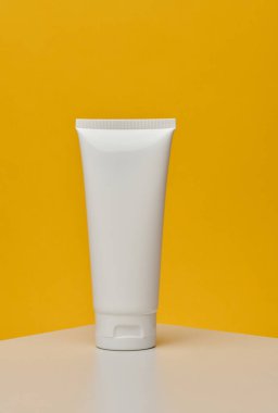 Diş macunu için beyaz plastik tüp, beyaz masa üzerinde kozmetik, sarı arka plan