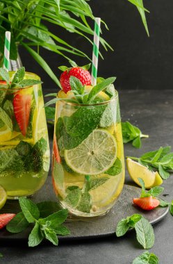 Limon dilimleri, çilekler, taze nane yaprakları ve köpüklü su dolu bir bardakta ferahlatıcı bir içecek.