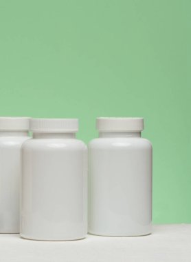 Yeşil arka planda hapları olan birkaç beyaz plastik kavanoz. Tıp ve sağlık hizmetleriyle ilgili eşyalar