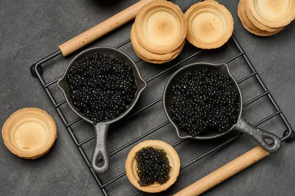 Siyah havyar ve boş yuvarlak turtalar siyah bir masanın üstünde.