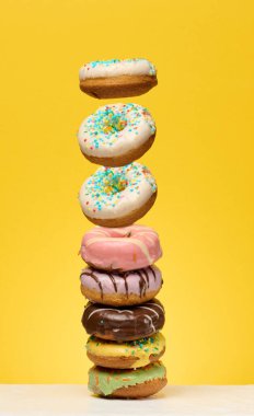 Beyaz bir yüzeye yerleştirilmiş, parlak sarı bir zemin üzerine çeşitli serpiştirilmiş ve çeşitli tasarımları olan uzun, dikey renkli donutlar..