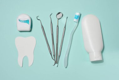 Beyaz diş macunu tüpü, beyaz kutuda diş ipi, diş aletleri ve mavi arka plana yerleştirilmiş beyaz dişler. Üst görünüm