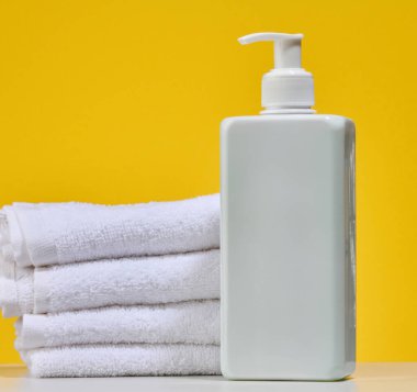 Beyaz kare şişe, şeker kutusu ve katlanmış beyaz havlu yığını, zengin sarı arka plan. Vücut bakımı veya spa tedavisi kavramı.