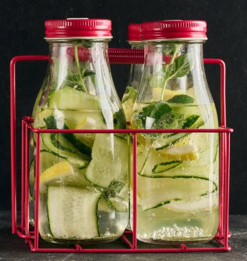 İçi salatalık, limon dilimleri ve nane yapraklarıyla dolu kırmızı kapaklı büyük şişeler.