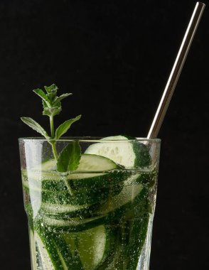 Bir bardak ferahlatıcı arınma suyu, salatalık dilimleri ve bir tutam nane, baloncuklu, koyu bir arka planda..