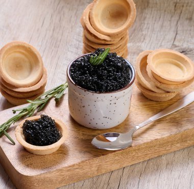 Seramik kapta siyah havyar ve tahta tahtaya yerleştirilmiş mini tart..