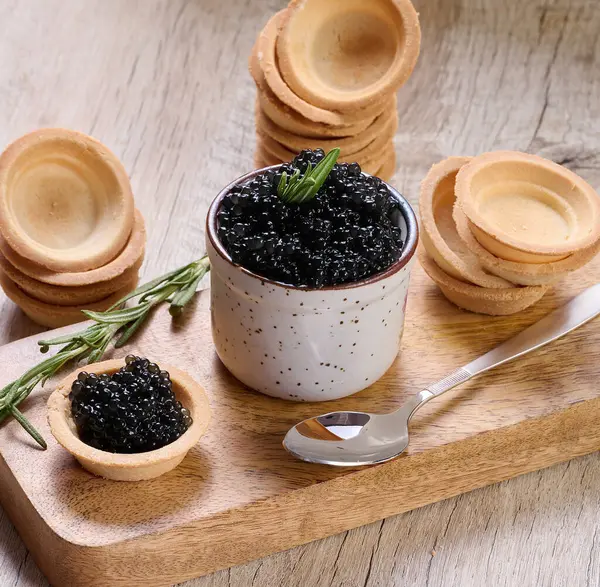 Seramik kapta siyah havyar ve tahta tahtaya yerleştirilmiş mini tart..