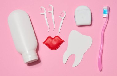 İki beyaz diş macunu, bir çantada diş ipi, diş ipi için plastik tutacağı, kırmızı dekoratif dudaklar, pembe arka planda iki diş fırçası. Üst görünüm.