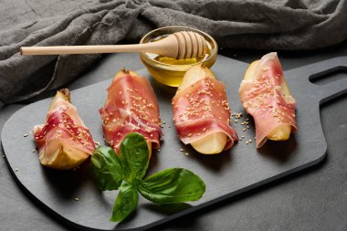 Prosciutto ve susam tohumlu armut aperatifi. Kara tahtada bal ile servis ediliyor.