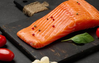 Siyah bir tahta üzerinde taze somon balığının yakın plan çekimi. Balığın zengin turuncu rengi ve kıtır kıtır bir dokusu vardır..