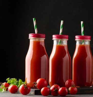 Siyah masanın üstünde domates suyu olan cam şişeler.