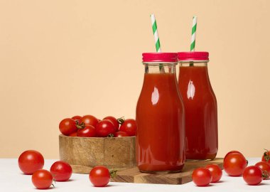 Kırmızı başlıklı domates suyu ile dolu cam şişeler. Taze kırmızı domatesler bir ahşap tezgahta ve önlerinde uzanır.