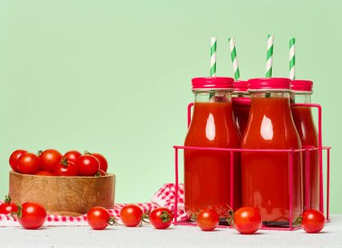Kırmızı metal bir stantta domates suyuyla doldurulmuş kırmızı başlıklı cam şişeler. Taze kiraz domatesleri ve yakınlarda bir yeşillik filizleri var.