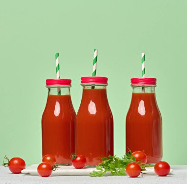 Domates suyuyla doldurulmuş ve yeşil çizgili kamışla süslenmiş kırmızı başlıklı cam şişeler. Yeşil arkaplan