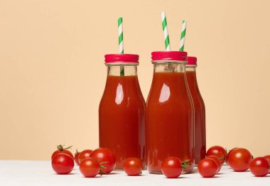Cam şişede domates suyu ve masada taze vişneli domates, bej arka plan.